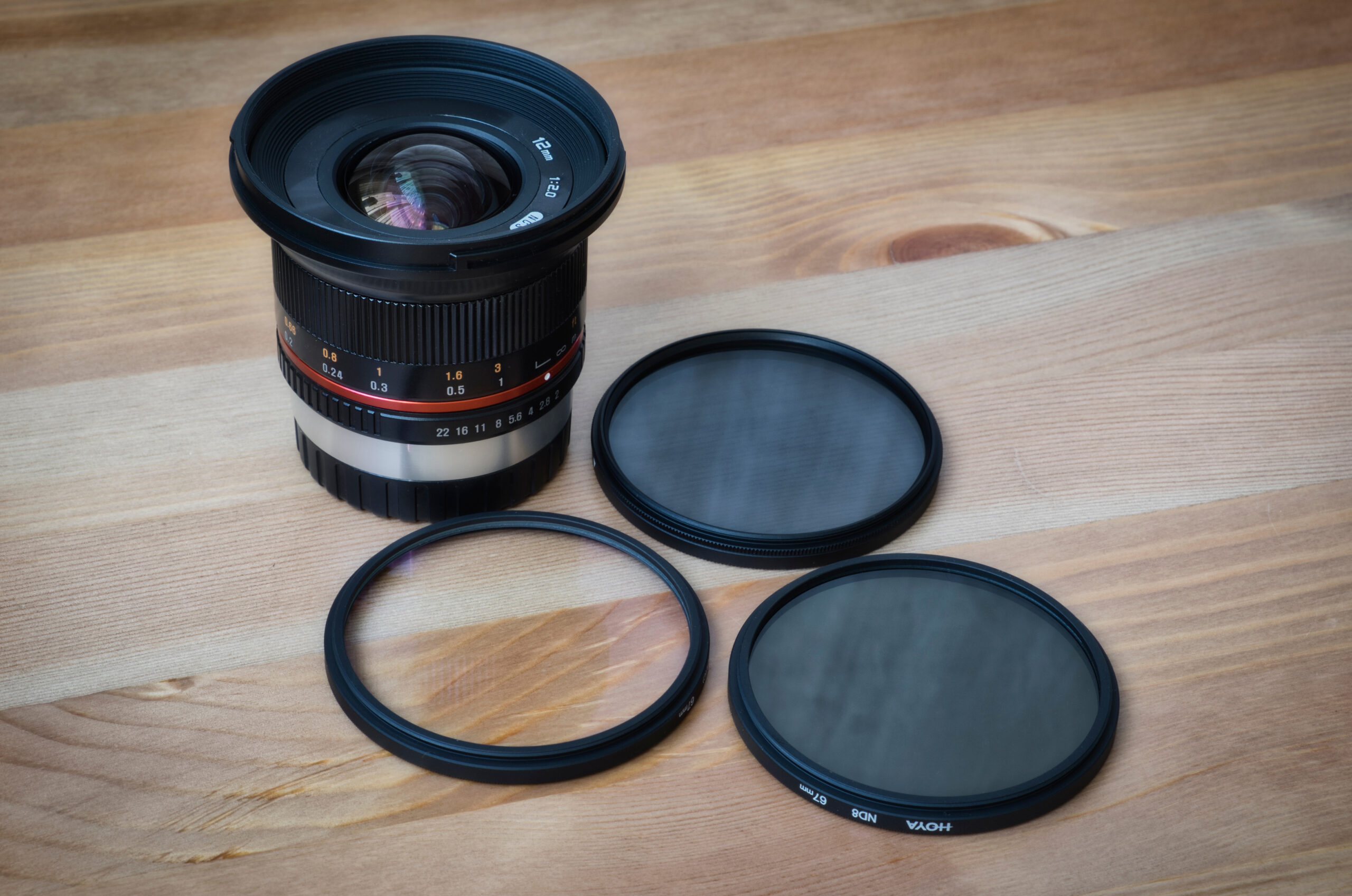 Moscow / Russia - may 27th 2020: Samyang 12mm f2 manual lens for fujifilm x-mount APSC cameras and Hoya filter kit laying on wood surface